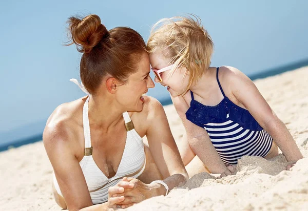 Mãe sorridente e criança de maiô brincando na praia — Fotografia de Stock