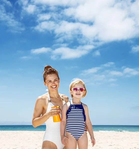 Gelukkig moeder toepassing van zonnebrandcrème op kind in zwembroek op het strand — Stockfoto