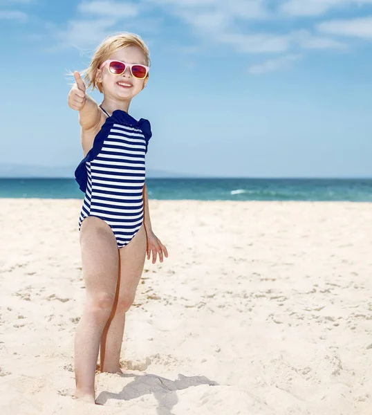 Glückliches Mädchen im Badeanzug an einem weißen Strand mit hochgereckten Daumen — Stockfoto