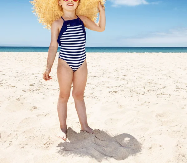 Счастливая девушка в полосатом купальнике и большой соломенной шляпе на белом пляже — стоковое фото