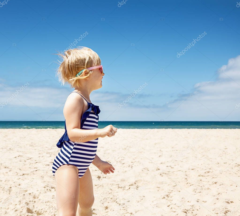 Happy girl in striped swimsuit on a white beach looking aside