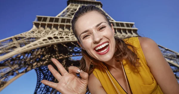 Usmívající se žena ukazuje ok gesto před Eiffel tower, Paříž — Stock fotografie