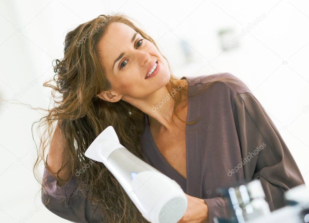 Happy young woman blow drying hair in bathroom