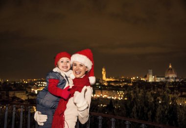 Gezi Floransa'da Noel anda ilham dolu. Genç anne ve kızı gezginler başparmak gösterilmesini Noel şapka önünde panoramik Floransa ile gülümseyen portresi