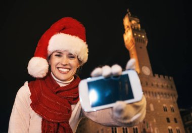 Gezi Floransa'da Noel anda ilham dolu. Floransa, İtalya gösteren smartphone'nın boş ekran Palazzo Vecchio karşı Noel şapka mutlu genç kadın portresi