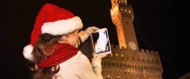 Gezi Floransa'da Noel anda ilham dolu. Floransa, İtalya alarak fotoğraf tablet Pc ile Noel şapka Palazzo Vecchio karşı genç turist kadının arkasından gördüm