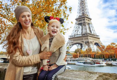 Mükemmel sonbahar tatil Disneyland ve Paris'te. Turistler anne ve kızı Minnie Fare kulağı setin yakınındaki parapetin üzerinde oturan Eyfel Kulesi Paris, Fransa'da içinde gülümseyen portresi
