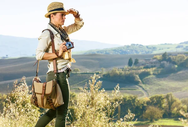 Tuscany büyülü manzarasını keşfetmek. Genç kadın ile mesafe içine vintage fotoğraf kamera ile Tuscany'de hiking çanta şapka uzun yürüyüşe çıkan kimse
