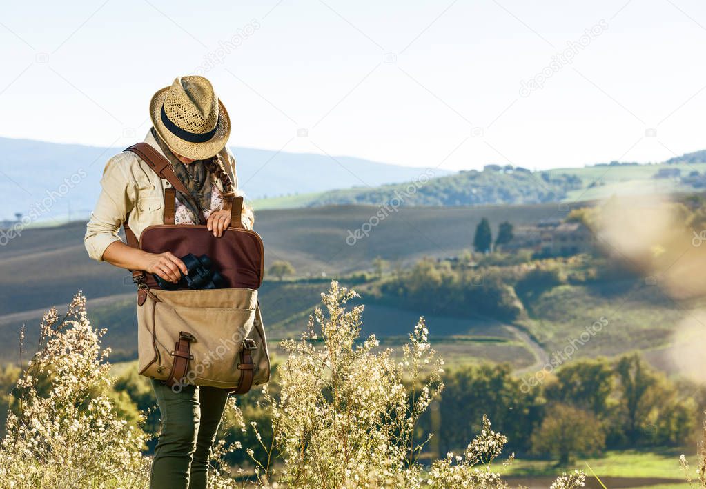 Discovering magical views of Tuscany. young woman hiker with bag hiking in Tuscany taking binoculars