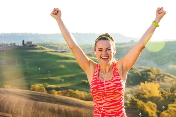 Fitness and magical views of Tuscany. Portrait of smiling active active woman in sports gear against scenery of Tuscany rejoicing