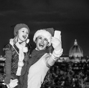 Gezi Floransa'da Noel anda ilham dolu. genç anne ve çocuk turist Noel şapka panoramik Floransa önünde selfie smartphone ile alarak gülümseyen