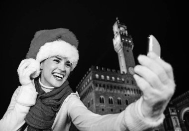 Gezi Floransa'da Noel anda ilham dolu. Noel şapkalı önünde Palazzo Vecchio, Florence, İtalya alarak selfie cep telefonu ile gülümseyen genç kadın portresi