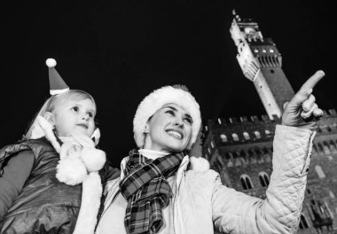 Gezi Floransa'da Noel anda ilham dolu. Modern anne ve Florence, İtalya bir şeye işaret içinde Noel şapka Palazzo Vecchio önünde kızı turist gülümseyen
