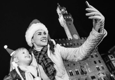 Gezi Floransa'da Noel anda ilham dolu. gülümseyen Genç Anne ve kızı turist Noel şapka Palazzo Vecchio Floransa, İtalya selfie cep telefonu ile alarak karşı