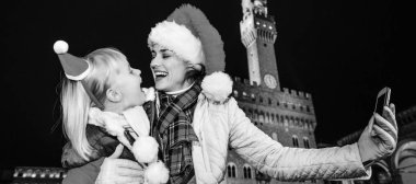 Gezi Floransa'da Noel anda ilham dolu. Modern anne ve sarılma ve selfie alarak çocuk gezginler ile Noel şapka Palazzo Vecchio karşı Floransa, İtalya gülümseyen