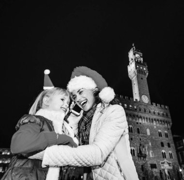Gezi Floransa'da Noel anda ilham dolu. Genç Anne ve kızı gezginler Floransa, İtalya Smartphone'da konuşmaktan Noel şapka Palazzo Vecchio karşı ile gülümseyen