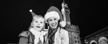 Gezi Floransa'da Noel anda ilham dolu. Neşeli Genç Anne ve kızı gezginler Palazzo Vecchio karşı Noel şapka ile Floransa, İtalya bir cep telefonu kullanarak portre