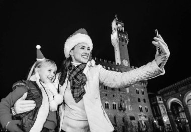 Gezi Floransa'da Noel anda ilham dolu. gülümseyen Genç Anne ve çocuk turist Noel şapka Palazzo Vecchio Floransa, İtalya ile telefon selfie alarak önünde