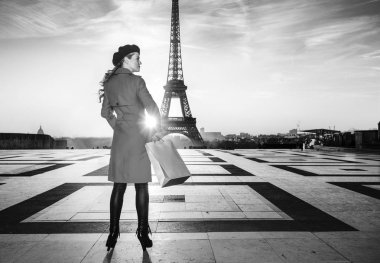 Paris'te parlak. Paris, Fransa'da kırmızı paltolu trendy turist kadın arkasından alışveriş çantası ile bir kenara seyir gördün mü