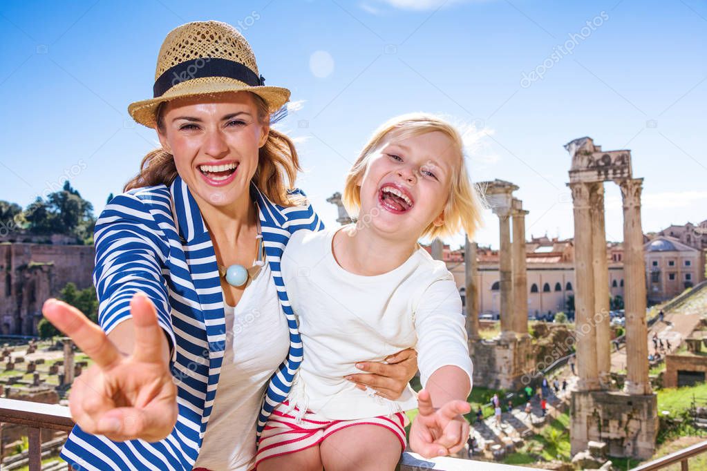 Roman Holiday. smiling trendy mother and daughter travellers against Roman Forum in Rome, Italy showing victory gesture