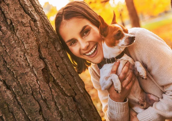 屋外から外を見ているツリーから秋の公園で犬と一緒に幸せな若い女 — ストック写真