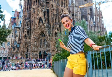 Barcelona - 10 Temmuz 2017: modern gezgin sarı şort ve Sagrada Familia için Barselona, İspanya, mesaj yazarken yakınındaki çizgili gömlek gülümseyen