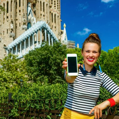 Barcelona - 10 Temmuz 2017: zarif gezgin kadın sarı şort ve Barcelona, İspanya gösteren smartphone boş ekran Sagrada Familia karşı çizgili gömlek