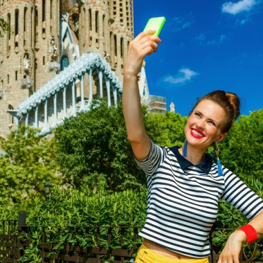 Barcelona - 10 Temmuz 2017: şık gezgin kadın sarı şort ve selfie alarak smartphone ile karşı Sagrada Familia için Barselona, İspanya, çizgili gömlek
