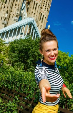 Barcelona - 10 Temmuz 2017: popüler turist kadın sarı şort ve Sagrada Familia için Barselona, İspanya, el için germe önünde çizgili gömlek