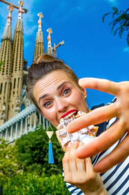 Genç turist kadın Sagrada Familia için Barselona, İspanya, ön tarafında çizgili gömlekli sağlıksız yiyecek zevk o görüntülenecek kadar istemiyor