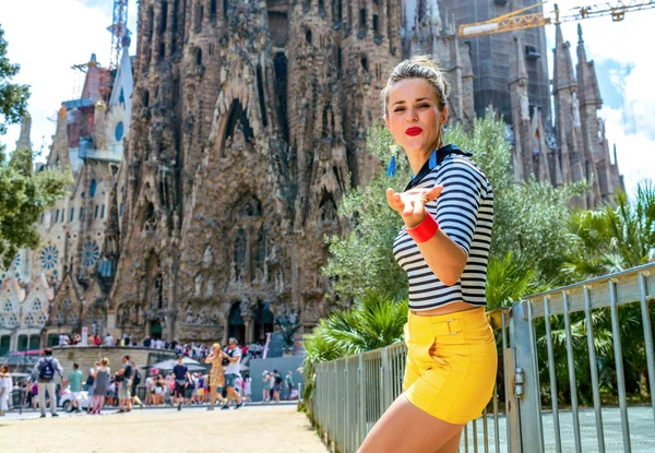黄色のショート パンツと空気キスを吹いてスペイン バルセロナのサグラダ ファミリアの前のストライプ シャツでバルセロナ 2017 幸せなトレンディな観光女性 — ストック写真