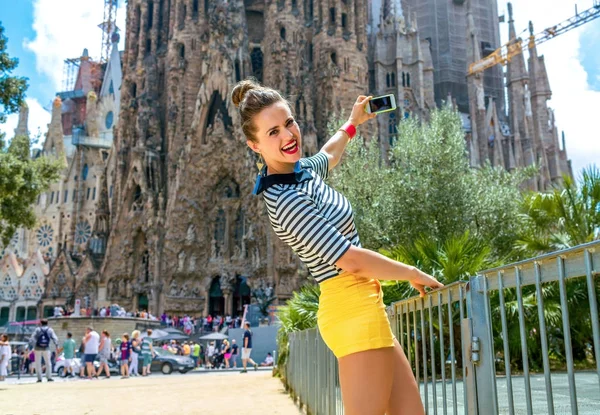 巴塞罗那 2017 快乐的年轻女子在黄色短裤和条纹衬衫反对圣家族在巴塞罗那 西班牙与电话拍照 — 图库照片