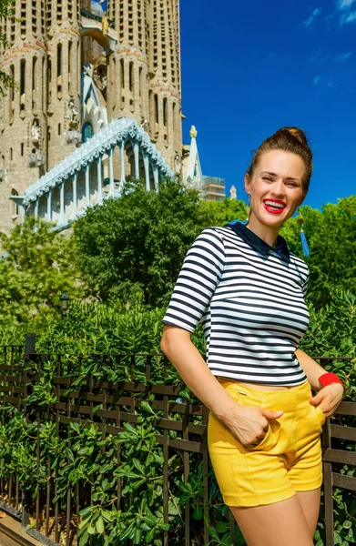 黄色のショート パンツとスペイン バルセロナのサグラダ ファミリアの前のストライプ シャツでトレンディな観光女性を笑顔のバルセロナ 2017 肖像画 — ストック写真