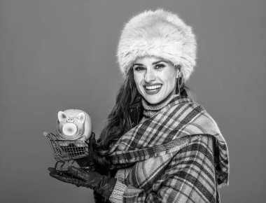 Kış şeyler. Kürk şapka kumbara ile alışveriş arabası tutan mutlu genç kadın portresi