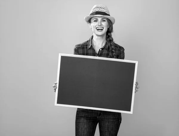 空白のボードを示す市松模様のシャツで若い女性生産者の笑顔のポートレート — ストック写真