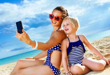 Güneş güzellik öptü. mutlu sağlıklı anne ve kızı deniz kıyısı ile selfie alarak dijital fotoğraf makinesi üzerinde mayo