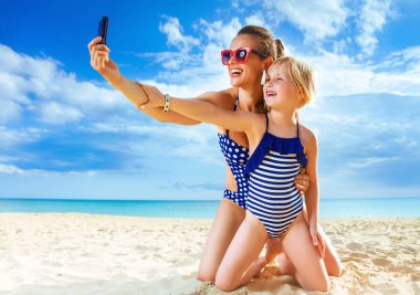 Güneş güzellik öptü. sağlıklı anne ve kızı beachwear sahil üzerinde selfie alarak dijital fotoğraf makinesi ile gülümseyen
