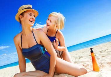 Güneş güzellik öptü. Genç Anne ve çocuk beachwear Spf uygulamak sahil üzerinde gülümseyen