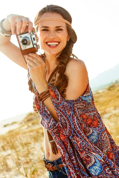 自由奔放な雰囲気のバカンス ジーンズのショート パンツと夏夜保持しているレトロな写真カメラで屋外岬で幸せなスタイリッシュな自由奔放に生きる少女 — ストック写真