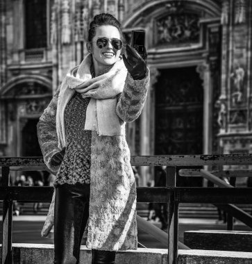 Modern gezgin kürk manto ve güneş gözlüğü Duomo Milan, İtalya önünde selfie alarak dijital fotoğraf makinesi ile gülümseyen tam uzunlukta portresi