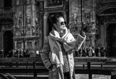modern gezgin kadın kürk manto ve Milan, İtalya katedral önünde güneş gözlüğü ile dijital fotoğraf makinesi alarak fotoğraf