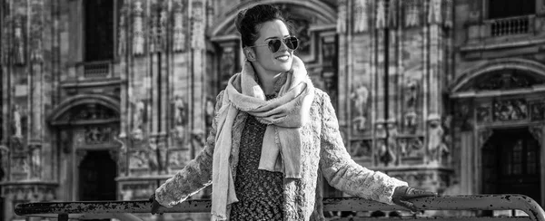 happy trendy woman in fur coat and sunglasses in the front of Duomo in Milan, Italy looking aside