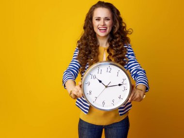 Trendy saat gösterilen sarı arka plan üzerinde uzun dalgalı esmer saçlı gülümseyen