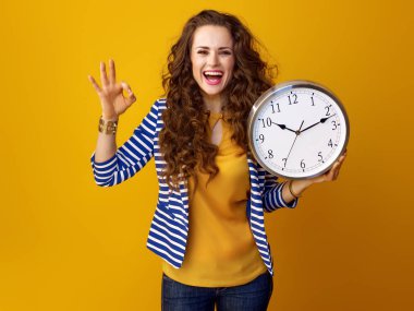 Trendy sarı zemin üzerine çizgili ceketli ok jest gösterilen saati ile gülümseyen