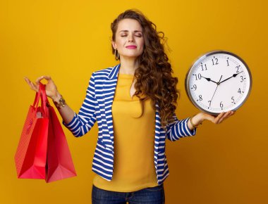 Saat ve kırmızı alışveriş torbaları gösterilen sarı arka plan üzerinde izole çizgili ceketli rahat moda kadın