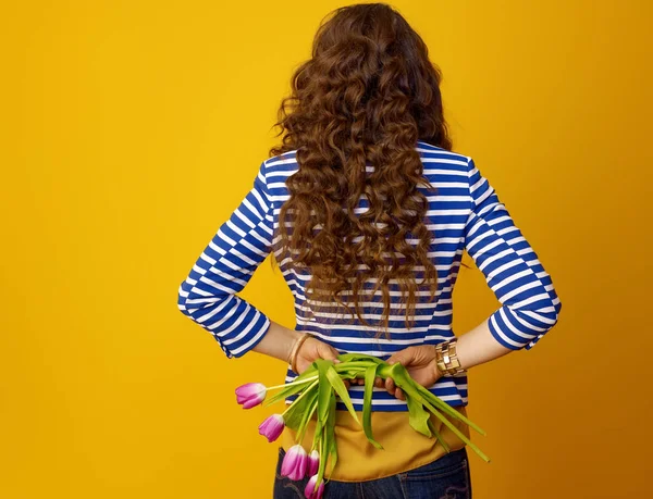 黄色の背景持株しおれた花に対して長い波状のブルネットの髪でトレンディな女性の後ろから見てください — ストック写真
