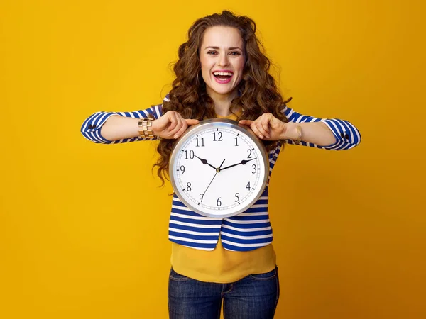 微笑时尚的妇女与长的波浪状黑发对黄色背景显示时钟 — 图库照片