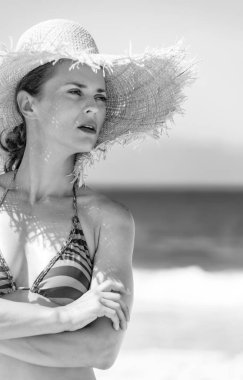 Mavi deniz, beyaz kum cenneti. Mesafe içine arayan sahil üzerinde beachwear ve saman şapkalı genç kadın portresi