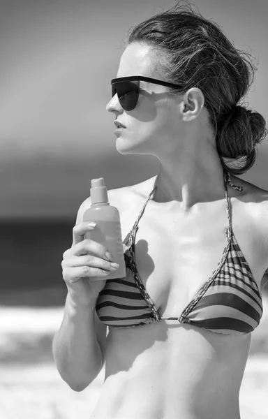 Blue sea, white sand paradise. Portrait of young woman in sunglasses and bikini on the seacoast with suntan lotion