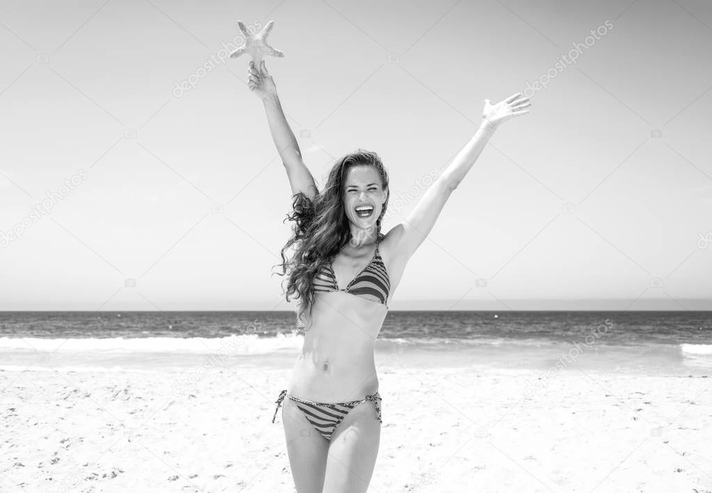 smiling young woman with long brunette hair in beachwear on the seacoast holding starfish rejoicing